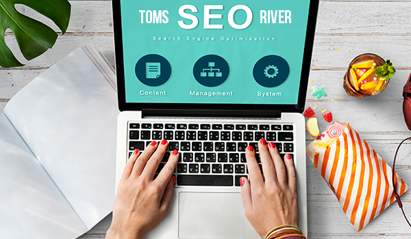 Toms River SEO on a teal screen of a laptop with hands on the keyboard